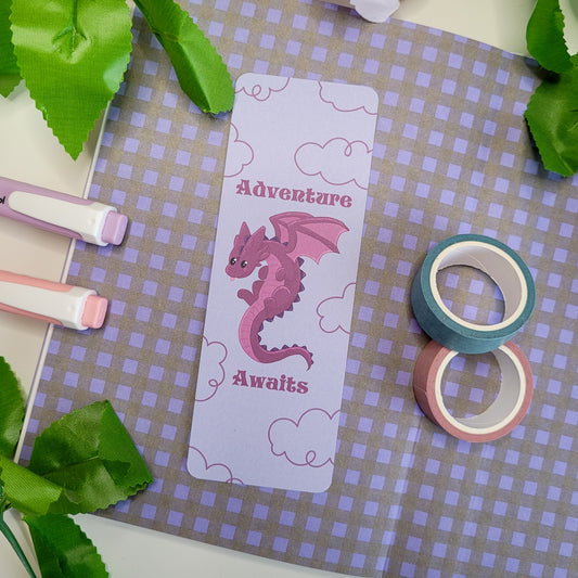 Cute purple dragron bookmark featuring clouds int he background and the text "Adventure Awaits"