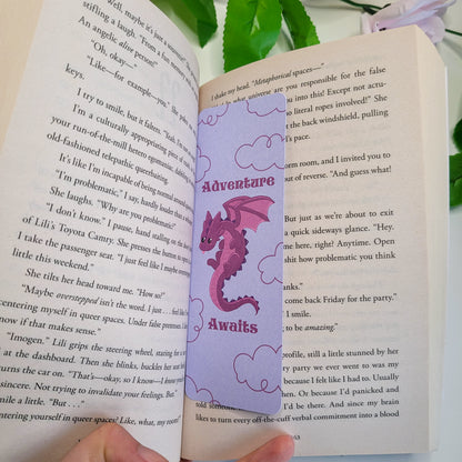 Cute purple dragron bookmark featuring clouds int he background and the text "Adventure Awaits"