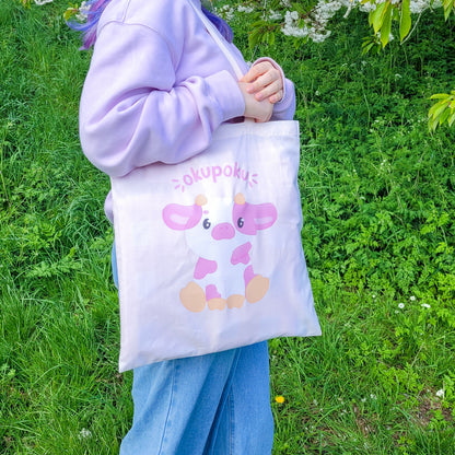 Light pink tote bag featuring an adorable pink cow design and the text okupoku