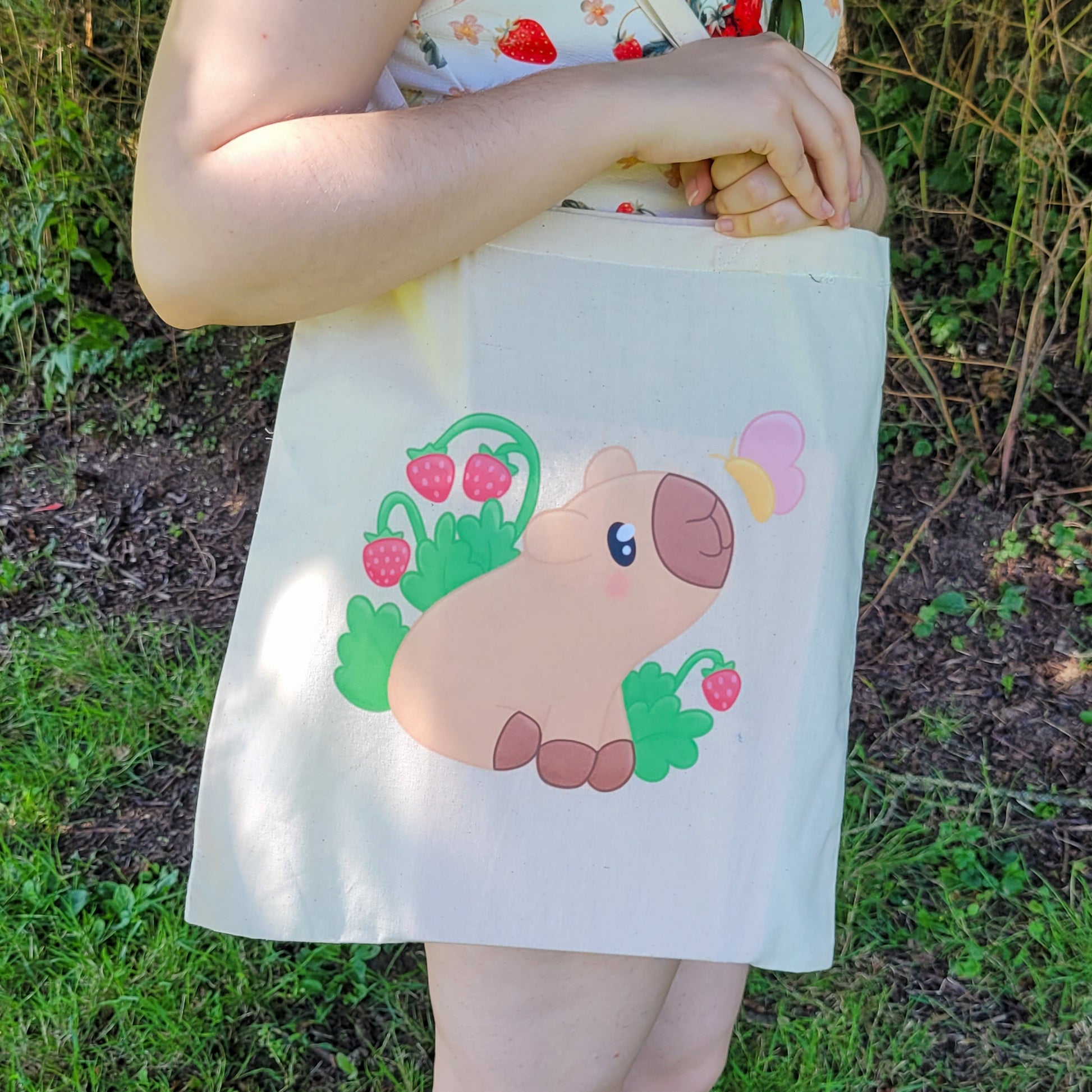 Natural colour tote bag featuring a cute capybara sitting with strawberries and a butterfly