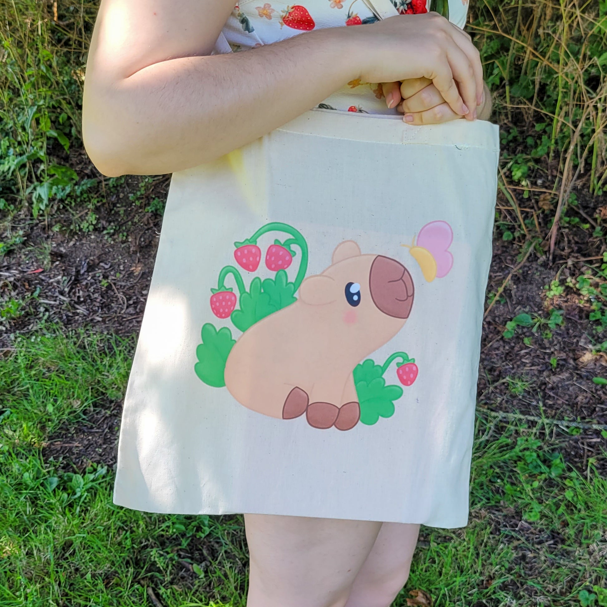 Natural colour tote bag featuring a cute capybara sitting with strawberries and a butterfly