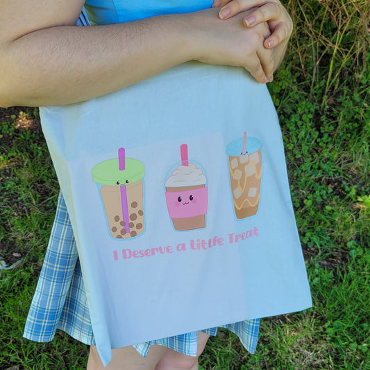 Light blue colour tote bag featuring a design of a bubble tea, frappucino and an iced latte with the text "I deserve a little treat"