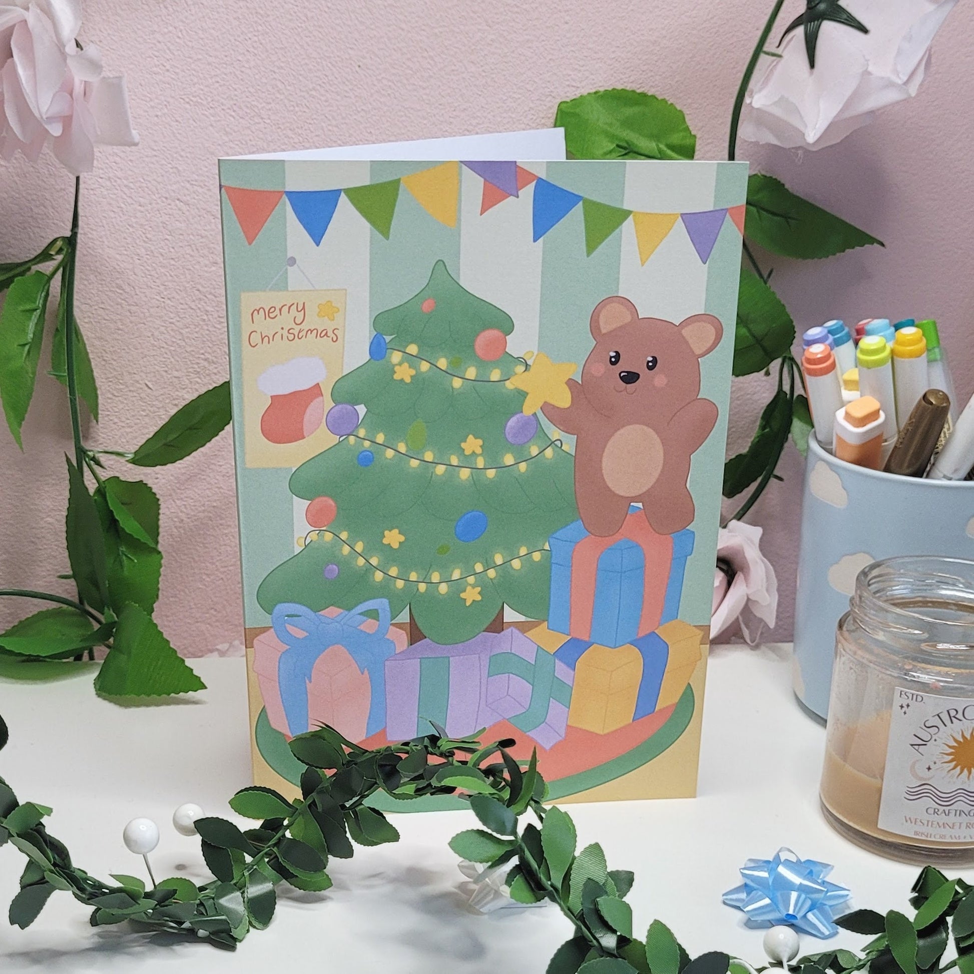 A cute christmas card featuring a little bear putting a star onto a christmas tree